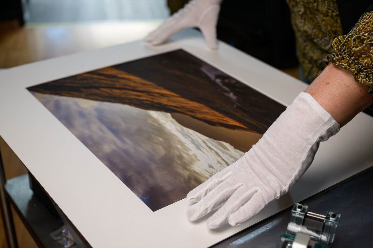 Des mains gantées ajustent un passe-partout autour d’un tirage dans notre atelier